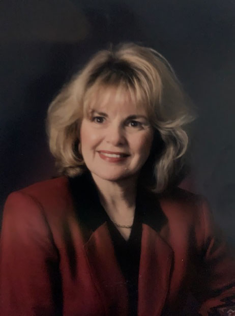 A portrait of a woman with blonde hair wearing a red suit.