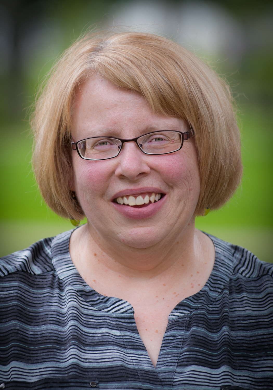 A headshot of a woman against a blurry green background. 