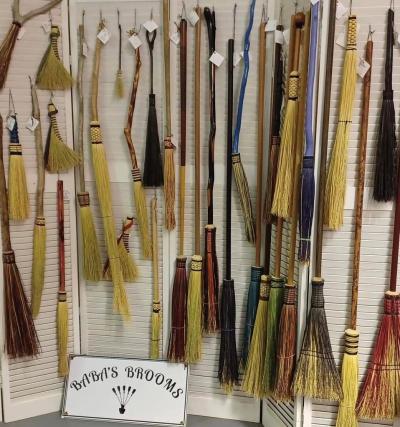 Image of brooms of different colors and sizes with a sign at the bottom that says 'Baba's Brooms'