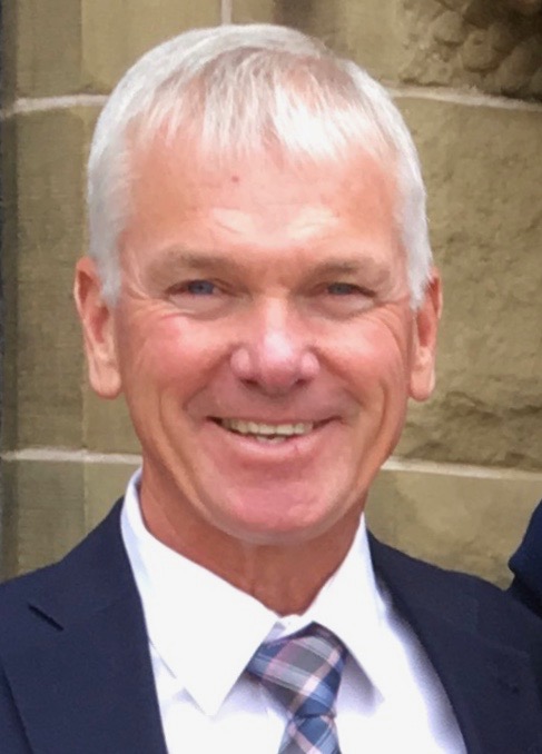A headshot of a smiling man wearing a navy suit and plaid tie.