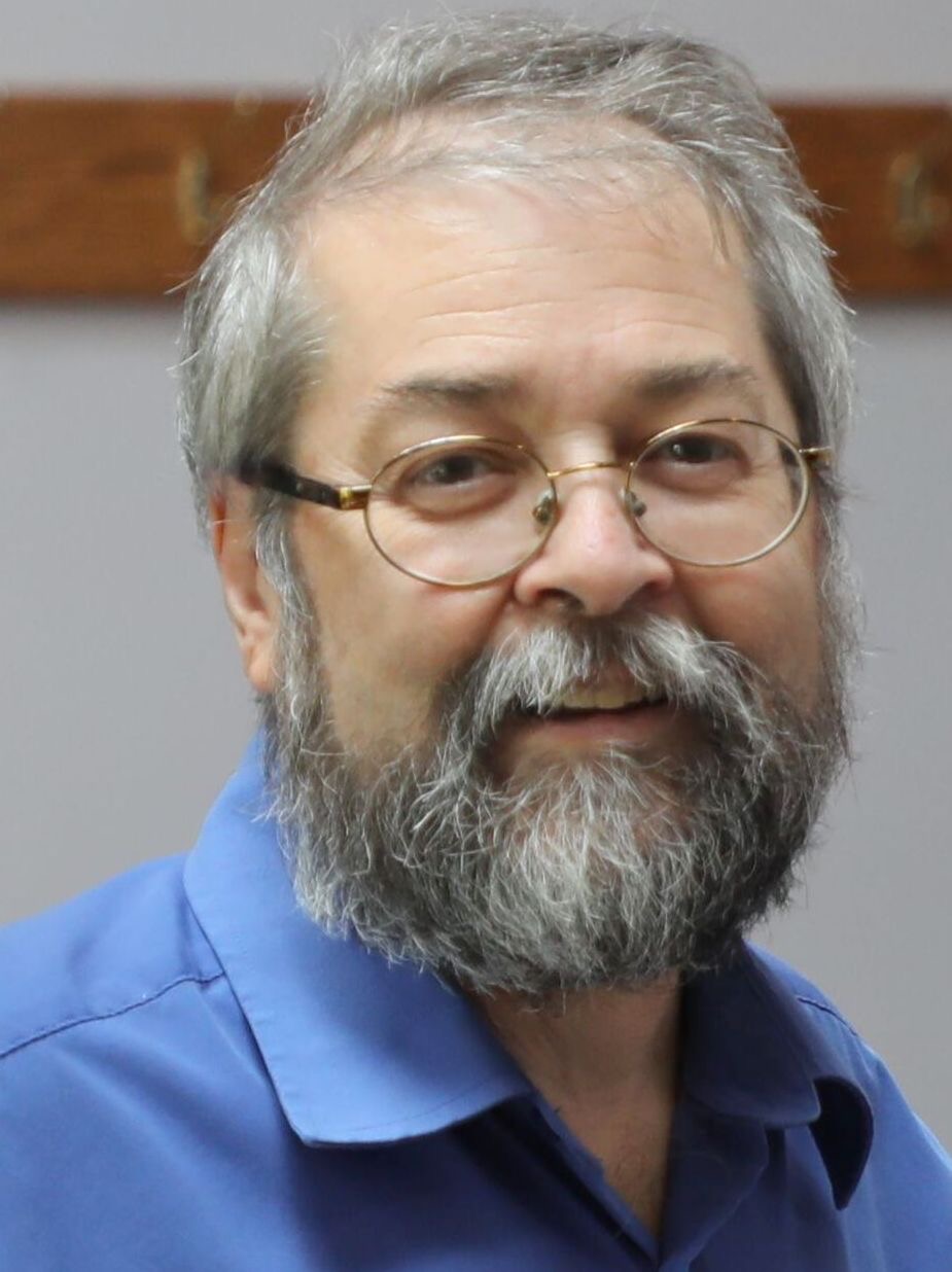 A headshot of a man wearing a blue collared shirt. 