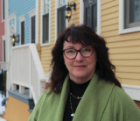 A smiling woman stands in front of a row of brightly coloured houses.