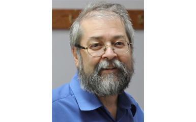 A head-and-shoulders photo of a man. He is wearing glasses and a blue collared shirt, and sports a greying beard.
